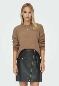 Maglione marrone a trama con maniche lunghe abbinato a una gonna in pelle nera caratterizzata da una cerniera laterale e dettagli con tasca frontale.
