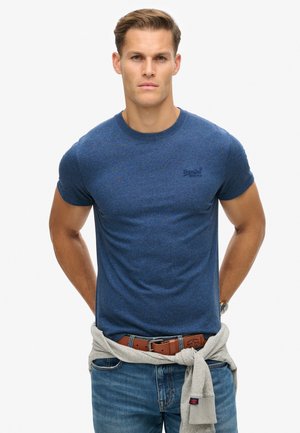 Camiseta de manga corta azul marino, con cuello redondo, tejido texturizado, con un pequeño logo en el pecho y un suéter gris claro atado a la cintura.