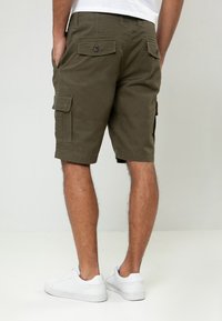 Shorts cargo vert olive en tissu durable, dotés de plusieurs poches et d'une coupe décontractée. Portés avec des baskets blanches.