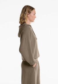 Brown hoodie with ribbed accents, drawstring hood, and relaxed fit. Model wears hands in pockets, pairing with matching joggers.