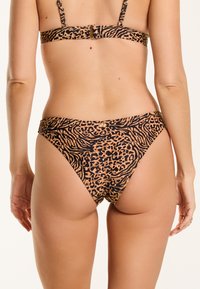 Leopardo rašto maudymosi kostiumėlis su juodos ir rudos spalvų deriniu, turintis plonas petnešas, užsegimą nugaroje ir žemai istoriją su lygia tekstūra.