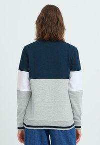 Felpa color blocco nei toni blu navale, grigio e bianco in tessuto morbido. Presenta maniche lunghe, polsini a costine e scollatura arrotondata.