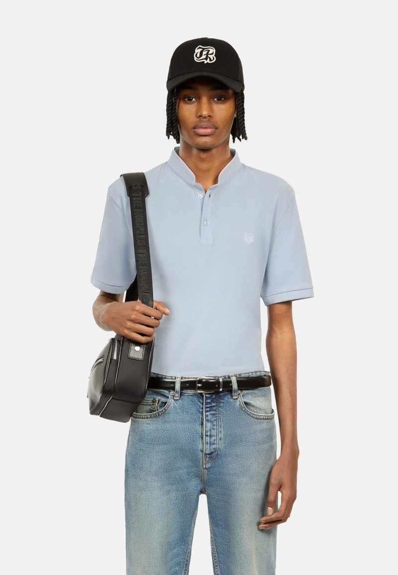 Polo shirt azzurro chiaro con colletto, abbinato a jeans sbiaditi a vita alta. Borsa a tracolla nera e cappellino con dettaglio del logo.