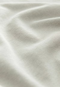 Lys beige stof med en glat, let tekstureret overflade, der viser naturlige folder og draperinger, som fremhæver dens bløde sammensætning.