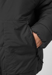 Giacca a vento nera con tasca con zip e orlo con cordino regolabile. Realizzata in materiale liscio e resistente all'acqua, con sezioni trapuntate.