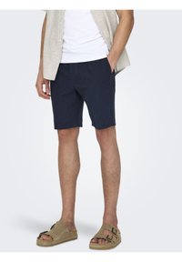 Marinede blå shorts laget av lett stoff, med rett snitt, sidelommer og sammen med beige sandaler.