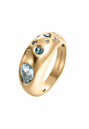 Anillo dorado con un diseño suave y redondeado que presenta varias gemas azules y claras, incluyendo una piedra central en forma de pera.