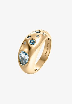 Anillo dorado con un diseño suave y redondeado que presenta varias gemas azules y claras, incluyendo una piedra central en forma de pera.