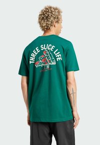 Vihreä puuvillainen t-paita, jossa on suuri grafiikka pizza-viipaleista, tomaateista ja valuva efekti. Yllä teksti "Kolme viipaleen elämä".