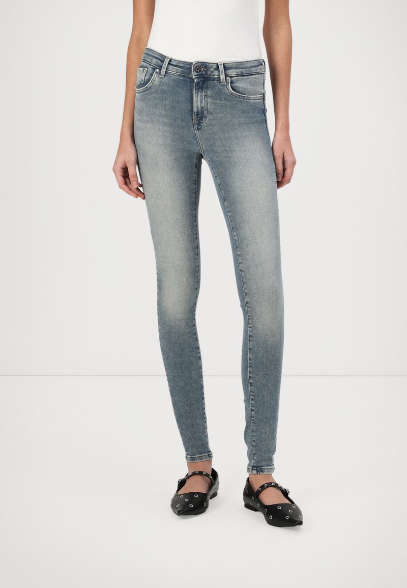 Jeans ajustados en denim azul claro, con una cintura de altura media, diseño clásico de cinco bolsillos y un ligero desvanecimiento. Combinados con bailarinas negras.