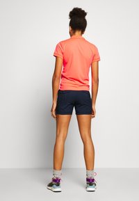 Polo de manga corta de color rosa brillante combinado con pantalones cortos navy, que cuentan con bolsillos traseros, y zapatillas grises con acentos coloridos y calcetines hasta el tobillo.