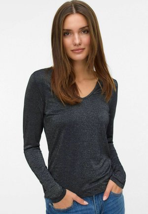 Zwart V-hals top met lange mouwen van een gestructureerde stof met dunne, horizontale metallic strepen. Model draagt het casual met blauwe jeans.