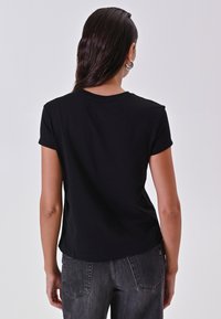 T-shirt nero a maniche corte realizzato in morbido cotone, con scollatura rotonda e orlo leggermente curvo. La vista posteriore mostra un design semplice.