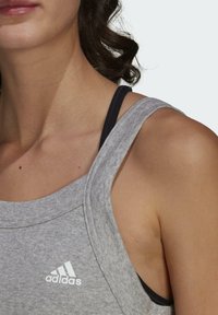 Débardeur de sport gris avec encolure dégagée et dos nageur. Logo Adidas blanc sur le côté gauche. Tissu doux et texturé.