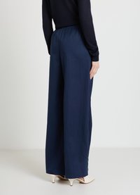 Weit geschnittene Hose aus marineblauem Stoff mit elastischem Bund, glatt strukturiert und mit dezenten Knopfakzenten an den Bündchen.