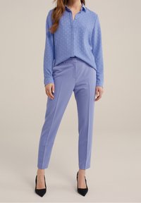 Ljusblå skjorta med knäppning och textur, i kombination med skräddarsydda ljuslila byxor och svarta högklackade skor.