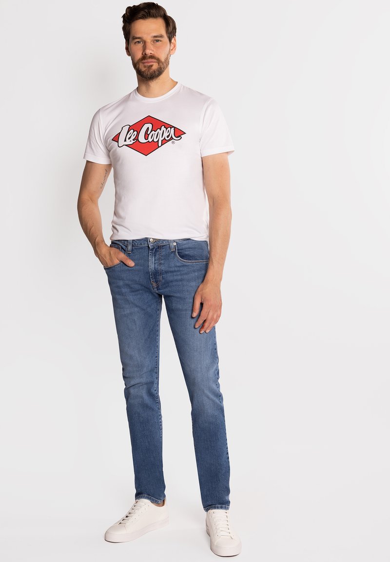 Biała koszulka z czerwonym logo "Lee Cooper", niebieskie jeansy i białe trampki. Dopasowany krój, krótkie rękawy, casualowy design, gładka bawełniana faktura.