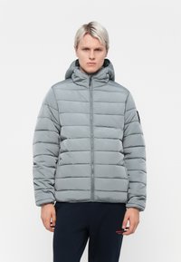 Lys grå pufferjakke med horisontal quiltet design, høj krave og fastgjort hætte, der har en kontrasterende sort sidelap.