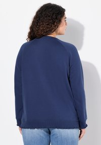 Felpa blu navy con vestibilità ampia, maniche raglan e finitura testurizzata. Presenta un colletto rotondo e orlo ondulato.