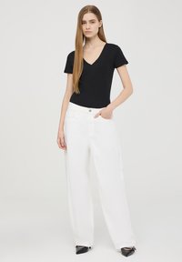 Body in vita a V nera a maniche corte abbinato a jeans bianchi a gamba larga. I jeans presentano una tasca frontale e una chiusura con bottone. Scarpe nere completano l'outfit.