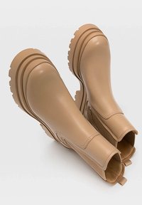 Bottines en cuir lisse de couleur tan avec un panneau latéral élastique texturé, semelle en caoutchouc épaisse et design à bout rond.