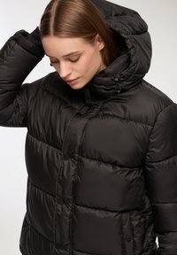 Czarna kurtka puchowa z kapturem, z pikowanym wzorem, zapinana na zatrzaski oraz ze ściąganym sznurkiem przy szyi.