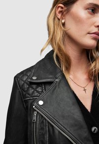 Giacca da biker in pelle nera con dettagli trapuntati sulle spalle, hardware argentato e zip asimmetrica. Accentuata da una finitura leggermente strutturata.