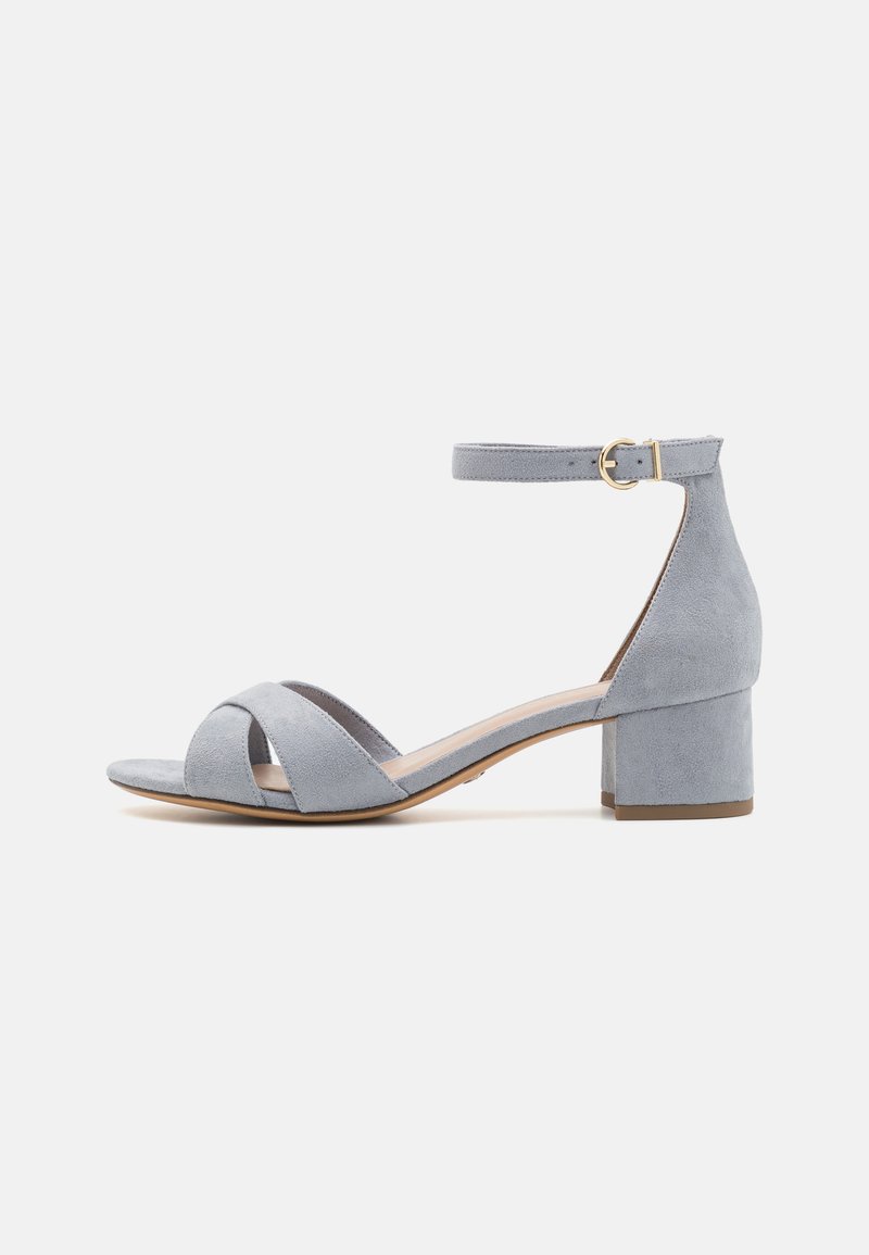 Grå mocka sandal med klack, utrustad med en ankelrem och korskorsad tådesign. Slät textur och minimalistisk stil.
