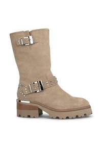 Bottes chelsea en daim beige avec un talon épais, quincaillerie en argent, accents cloutés et une sangle décorative. Semelle en caoutchouc avec traction.