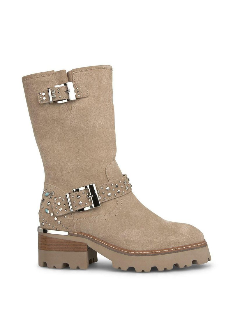 Bottes chelsea en daim beige avec un talon épais, quincaillerie en argent, accents cloutés et une sangle décorative. Semelle en caoutchouc avec traction.