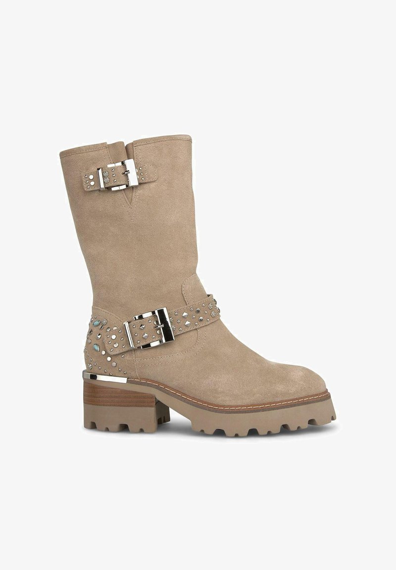 Bottes chelsea en daim beige avec un talon épais, quincaillerie en argent, accents cloutés et une sangle décorative. Semelle en caoutchouc avec traction.
