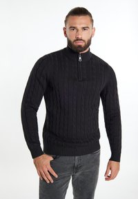 Pullover nero in maglia con colletto alto, dotato di zip a metà e motivo a treccia. Design aderente con polsini e orlo a costine.