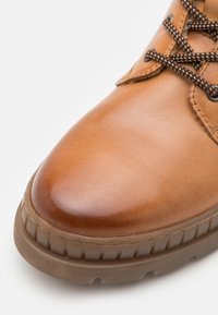 Stivaletto in pelle marrone con finitura liscia, punta tonda e lacci marroni in contrasto. La suola in gomma presenta un design battistrada.