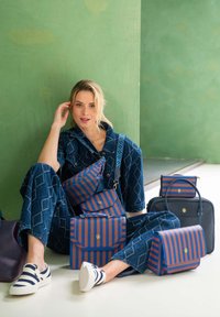 Kollektion von Taschen in blauen und orangefarbenen Streifen, aus strapazierfähigem Material gefertigt, die verschiedene Formen präsentieren: Umhängetasche, Tragetasche und Clutch.