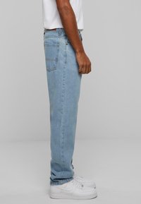 Light blue straight-leg jeans made of denim, featuring a classic five-pocket design and a slight fade. Styled with white sneakers.