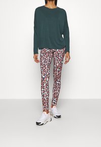 Mörkgrön långärmad topp, lös passform; tajta leggings med rosa och svart leopardmönster; vita sneakers med orange detaljer.