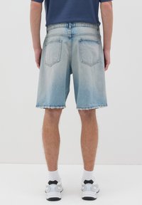 Pantalones cortos de mezclilla de color azul claro con un dobladillo deshilachado, dos bolsillos traseros y un corte relajado. Combinados con zapatillas blancas y calcetines hasta el tobillo.