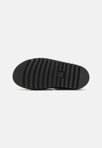 Suela de zapato de goma negra con estrías horizontales y agarre texturizado, que presenta un logo central y una zona de punta curvada para la continuidad del diseño.