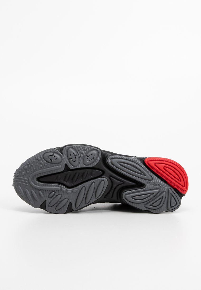 Sohle eines schwarz-grauen Sportschuhs mit strukturierten Mustern und einem roten Gummibereich an der Ferse, Adidas-Logo an der Seite sichtbar.