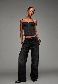 Schwarzes Leopardenmuster-Peplum-Top mit dünnen Trägern, kombiniert mit locker sitzenden, dunkelblauen Jeans und spitzen schwarzen Absätzen. Minimale Schmuckakzente.