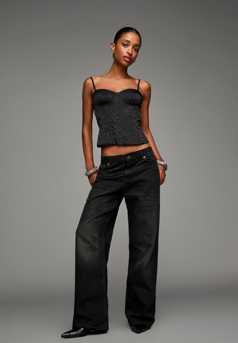Schwarzes Leopardenmuster-Peplum-Top mit dünnen Trägern, kombiniert mit locker sitzenden, dunkelblauen Jeans und spitzen schwarzen Absätzen. Minimale Schmuckakzente.