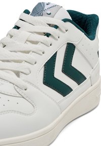 Białe skórzane sneakersy z ciemnozielonymi akcentami. Do cech należy teksturowany język, wyraźne logo oraz perforowane detale po bokach.