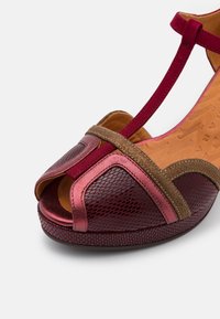 Sandale ouverte pour femme avec un mesh bordeaux, des accents en daim rose métallique et marron, et une bride en T rouge sur une semelle beige.