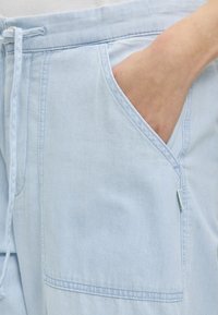 Χέρι τοποθετημένο στην μπροστινή τσέπη ανοιχτόχρωμου τζιν παντελονιού με κορδονάτο μήκος μέσης και εμφανείς ραφές.