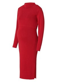 Robe de maternité en tricot rouge, à manches longues, col montant et silhouette ajustée avec une fente latérale pour faciliter les mouvements.