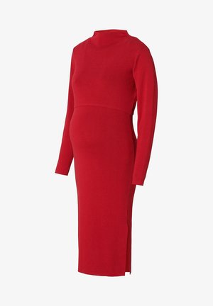 Robe de maternité en tricot rouge, à manches longues, col montant et silhouette ajustée avec une fente latérale pour faciliter les mouvements.