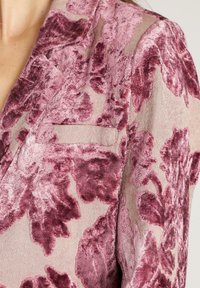 Blazer de terciopelo en rosa empolvado con grandes patrones florales en burdeos oscuro. Presenta un acabado texturizado y un único bolsillo en el pecho.