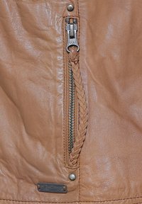 Bruine leren jas voorzien van een metalen YKK-rits met een gevlochten accent, een klein metalen logo plaatje en een textuur oppervlak.