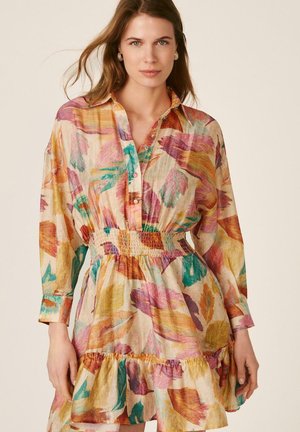 Mujer con un vestido de manga larga abotonado, con un patrón abstracto de hojas coloridas y una cintura elástica fruncida.