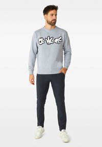 Sudadera gris con diseños gráficos negros, puños y dobladillo texturizados; combinada con pantalones de canalé en azul marino y zapatillas blancas.